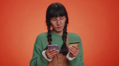 Samimi inek kadın müşteri kredi kartı ve akıllı telefon kullanarak para transferi, online alışveriş, ödeme yapıyor. Finans ve internet. Genç kız turuncu arka planda tek başına.