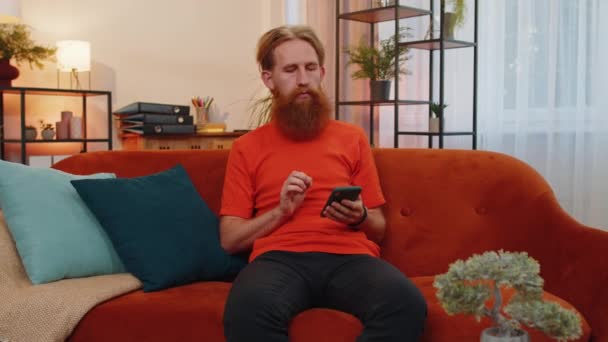 Portrait Homme Barbu Assis Sur Canapé Utilise Sourire Téléphonie Mobile — Video
