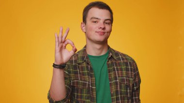 Tişörtlü bir adamın kameraya onaylı geri bildirim jesti göstermesi sevindirici. Stüdyonun sarı arka planında genç bir çocuk. İnsanlar samimi duygular