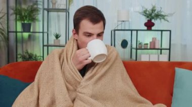 Hasta ergen erkek öğrenci kanepede soğuktan titreyerek ekoseye sarılmış borç krizi yüzünden ısınmadan sıcak çay içiyor. Sağlıksız genç adam kendini rahatsız hissediyor.