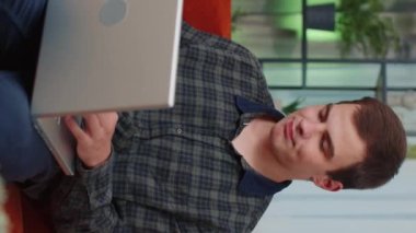Genç adam dizüstü bilgisayar kullanır, iyi haber mesajı alır, ani zaferle şok olur, piyango kazananını kutlar, evden online alışveriş yapar. Dikey görüntü. İnanılmaz mutlu, şanslı adam.