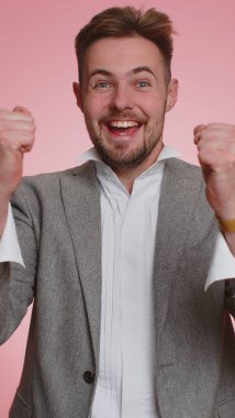 Mutlu iş adamları bağırıyor, el kol hareketi yapıyor başarıyı kutluyorum, kazanıyorum, doğum günü, piyango hedefini başarıyla tutturuyorum. Yetişkin erkek çocuk pembe stüdyo arka planında. Dikey