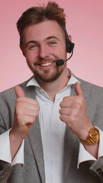 Business man wearing headset, freelance worker, call center or support service operator helpline, having talk with client or colleague communication support. Young guy on pink background. Vertical