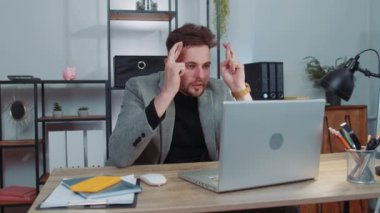 Concentrated businessman winner in suit working on laptop at home office desk typing browsing say Wow yes found out great big lottery win good news celebrate. Male manager freelancer man occupation