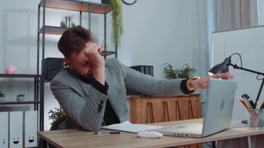 Businessman in suit working on laptop computer, meditating, doing yoga breathing exercise in lotus position at home office desk. Calm serene freelancer man taking break. Busy occupation. Peace of mind