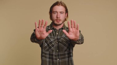 No stop. Serious adult man say No, hold palm folded crossed hands in stop danger gesture, warning of finish, prohibited access, declining communication, body language. Young guy on beige background