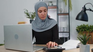 Finansal belge faturalarıyla çalışan tesettürlü genç Müslüman iş kadını, grafikler ve gelir grafiği raporları için vergileri hesaplıyor. Modern ofis çalışma alanında serbest çalışan kız evrakları.