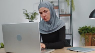 Başı ağrıyan, baş ağrısı, migren ve stresten muzdarip tesettür kullanan tesettürlü Müslüman iş kadını. Kız serbest yazar, defter üzerinde çalışır, mesajlar gönderir, internet üzerinden alışveriş yapar.