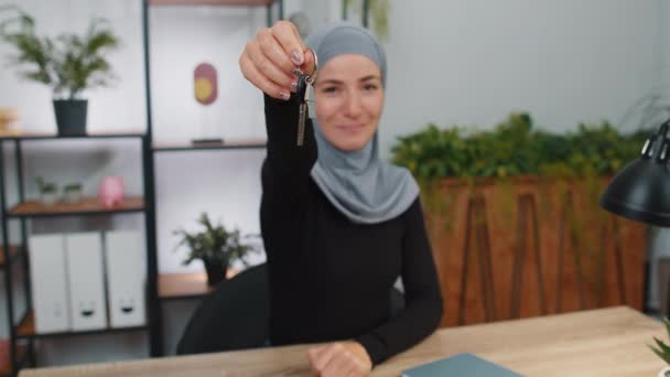若いイスラム教徒のビジネス女性は 新しい家のアパートの鍵を示す手を持ち上げるヒジャーブ不動産屋を着て 不動産 住宅ローンを購入または賃貸します 現代のホームオフィスワークスペースの女の子 — ストック動画