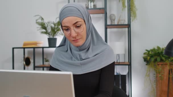 在总部完成笔记本电脑工作后 穿着头巾的女商人看着相机 戴着眼镜微笑的穆斯林自由职业者女孩忙着上网工作 做着遥远的工作 笔记本上的电子学习互联网 — 图库视频影像