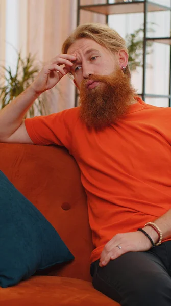 stock image Portrait of sad lonely man sitting at home looks pensive thinks over life concerns or unrequited love, suffers from unfair situation. Young guy problem, break up, depressed feeling bad annoyed burnout