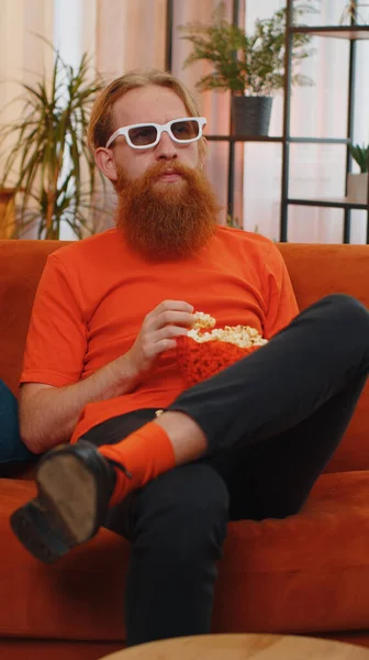 大胡子兴奋年轻人的肖像坐在沙发上吃爆米花 在家里看有趣的电视连续剧 体育游戏 在线社交媒体电影内容 享受家庭娱乐的男人 — 图库照片