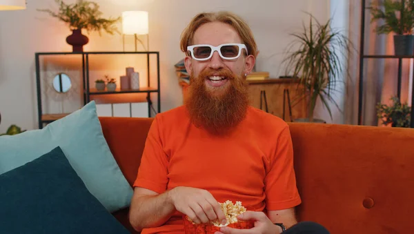 红头发兴奋的年轻人的肖像坐在沙发上吃爆米花 在家里看有趣的电视连续剧 体育游戏 在线社交媒体电影内容 享受家庭娱乐的男人 — 图库照片