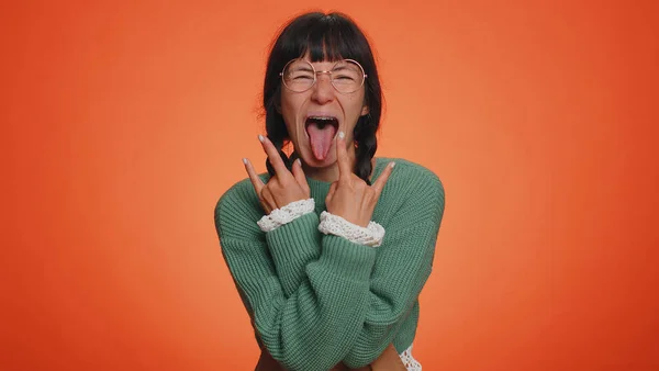 Rock n roll. Overjoyed delighted woman 30 years old in sweater showing gesture by hands, cool sign, shouting yeah with crazy expression, dancing, emotionally rejoicing in success win on orange wall