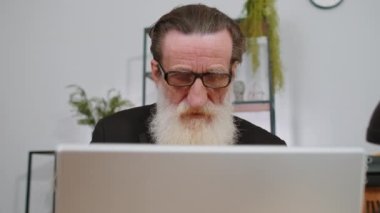 Yakın plan portre, iş yerinde dizüstü bilgisayarla çalışan kıdemli iş adamı büyükbaba Freelancer 'a ait. Yönetici serbest çalışan yaşlı bir adam defter üzerinde çalışır mesajlar gönderir çevrimiçi alışverişler yapar