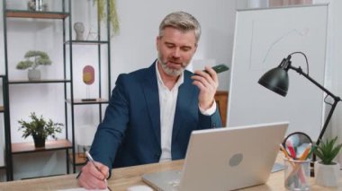 Olgun iş adamı çalışıyor, cep telefonu hoparlörleri ofiste dizüstü bilgisayarla konuşuyor. Kurye sohbet uygulamaları kullanarak akıllı telefon tutan, serbest çalışan yaşlı bir yönetici. İstihdam, meslek