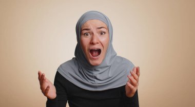 Aman Tanrım, vay canına. Heyecanlı Müslüman kadın şaşkınlıkla el kaldırıyor büyük gözlerle kameraya bakıyor, ani zaferden şok oluyor. Samimi genç kız bej renkli stüdyo arka planında tek başına.