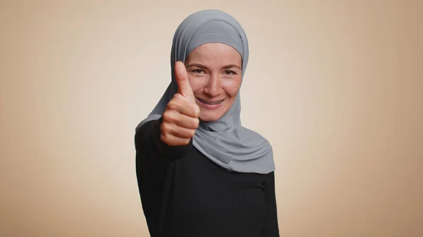 希斯特穆斯林妇女在头巾中竖起大拇指同意某事或给予肯定的回答 推荐广告喜欢好的 在米色工作室背景下孤身一人的阿拉伯女孩 — 图库照片
