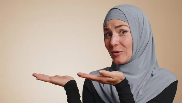 ヒジャーブ州のイスラム教徒の千年紀の女性が親指を立てて空の場所 商業テキストの広告エリア 商品プロモーションのためのコピースペースを指しています 若い娘だ スタジオ撮影室内でベージュの背景 — ストック写真
