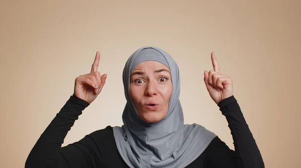 ヒジャーブのイスラム教徒の女性が親指を立てて空の場所 商業テキストの広告エリア 商品プロモーションのためのコピースペースを指しています 若い大人の女の子 室内スタジオショット上のベージュの壁の背景 — ストック写真