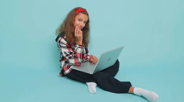 快乐的青少年小女孩12岁的时候在笔记本电脑上工作 发送消息 在网上购物 看电影 独自坐在工作室蓝色背景上的十几岁以下儿童 — 图库照片