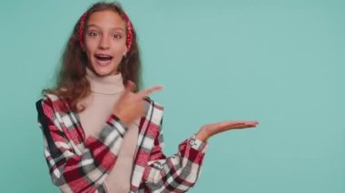 12 yaşında mutlu bir kız çocuğu boş bir yeri işaret ediyor. Ticari metinler için reklam alanı, ürün tanıtımı için kopya alanı. Genç bir çocuk. Mavi duvar arkaplanındaki stüdyo görüntüleri