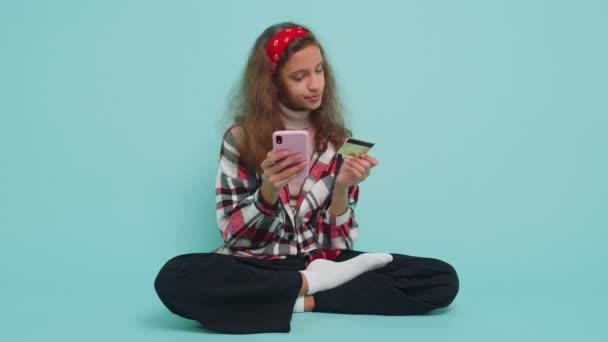 十几岁的小女孩在汇款 网上购物 订购食品时使用信用卡和智能手机 未成年的孩子们坐在工作室的蓝色背景上 — 图库视频影像