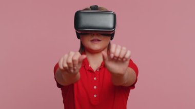Çevrimiçi oyun uygulaması oynamak için kulaklık kullanan genç bir kadın. Sanal gerçeklik 3D 360 video içeriği izliyor. Stüdyo pembe arka planda VR gözlüklü beyaz bir kız. Gelecekçi teknoloji