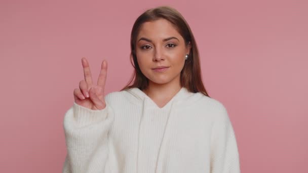 勝利Vサインを示す白いセーターのヒップスター女性は 成功と勝利を期待し 平和のジェスチャーを行い 一種の楽観的な表現で笑顔 若いです大人女の子絶縁上のピンクスタジオ背景 — ストック動画