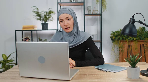 Business woman wearing hijab working on laptop computer at home office desk talk on online communication video call with employee client, boss. Muslim student girl freelancer customer support services