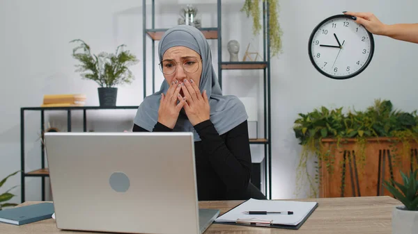 Business woman programmer software developer working on laptop at office with anxiety checking time on clock, being in delay, deadline. Concentrated muslim freelancer business girl worrying to be late