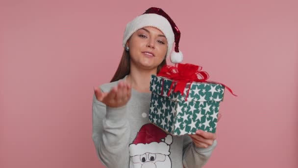 年轻的女人穿着圣诞老人的毛衣开心地笑着庆祝圣诞节 礼物盒给了相机一个惊喜 她伸出双手 在粉红工作室背景上被隔离的女孩 — 图库视频影像