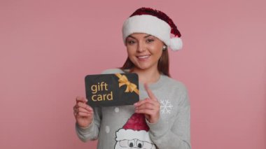 Noel Baba kazaklı kadın bayramları kutluyor. Hediye indirimi kuponu göstererek bayram indirimi yapıyor. Pembe arka planda Noel sürprizi kartı olan kız.