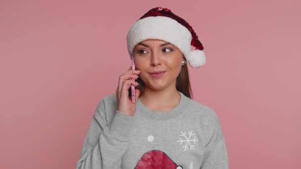 身穿圣诞老人毛衣的年轻女子庆祝圣诞假期 与朋友通电话 致以最良好的祝愿 喜欢在粉红工作室背景下与他人单独交谈的女孩 — 图库视频影像