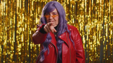 Hey sen! 70 'li yaşlarda ceketli bir kadın heyecanlı bir şekilde gülümsüyor ve kamerayı işaret ediyor. Şanslı piyango talihlisini seçiyor. Parlak disko partisinin arka planında yaşlı bir büyükanne izole edilmiş.