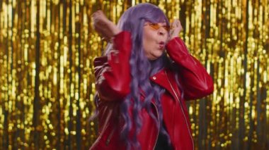 Mor saçlı bir kadın stres gerginliği yüzünden çığlık atıyor. Korku, umutsuzluk, şaşkınlık, şaşkınlık, öfke belirtileri gösteriyor. Yaşlı büyükanne, parlak disko partisi folyo arka planında izole edilmiş.