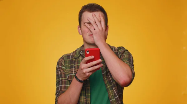 シャツの10代の男性は 携帯電話の携帯電話のブラウジングを使用して 突然宝くじの結果 失敗に驚いて失う 若いです大人男男の子絶縁一人で黄色のスタジオ壁の背景 — ストック写真