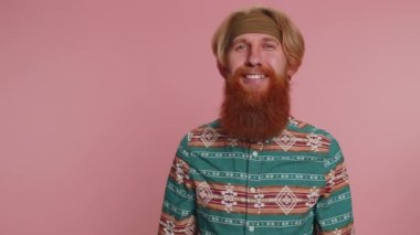 Neşeli hippi sakallı, şablon gömlekli kızıl adam kameraya bakıp gülümsüyor. Genç moda stili hippi erkek. Stüdyodaki kızıl saçlı erkek. Pembe duvar arkasında izole edilmiş. Erkek doğası güzelliği