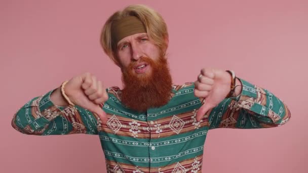 嫌いだ 嫌いを表現し サインジェスチャーを親指を示すパターンシャツの不幸なヒッピーの男を動揺 若い赤毛の男だ ピンクの背景で撮影された屋内スタジオ — ストック動画