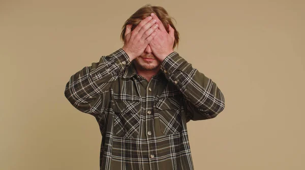 Dont want to look at this, awful. Handsome shocked bearded man closing eyes with hand showing stop gesture, confused shy scared to watch. Young adult guy boy isolated alone on beige studio background