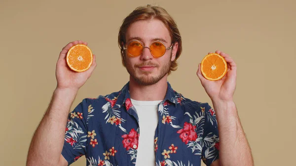 ハンサムな観光の若者の目にオレンジの半分を入れて 菜食主義の生活様式 健康のためのビタミン 幸せな休暇の休日 有機エコ食品 若いです男男の子絶縁上のベージュスタジオ壁の背景 — ストック写真