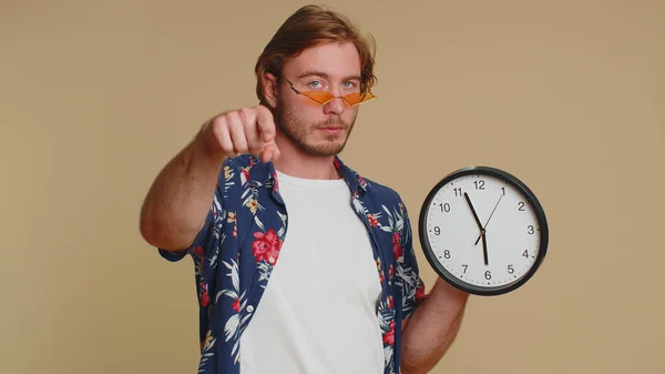 这是你的时间 穿着衬衫 留着胡子的年轻人的画像 在钟表上显示时间 竖起大拇指 用手指对着相机 在室内拍摄的一个成年人在米色背景下被单独拍摄 — 图库照片