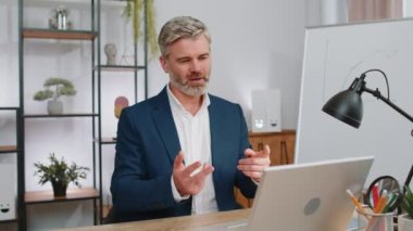 Ev ofisinin bilgisayarında çalışan olgun bir iş adamı çalışanlarıyla online haberleşme videosu hakkında konuşuyor, patron. Yönetici gri saçlı yaşlı adam serbest çalışan destek servisleri kameraya bakıyor.