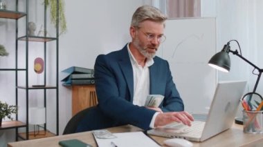 Bilgisayarda çalışan zengin, olgun bir iş adamı nakit para sayıyor, işyerindeki gelir gelirlerini hesaplıyor. Profesyonel menajer serbest çalışan adam. İş dünyası yaşlıları. İstihdam, meslek