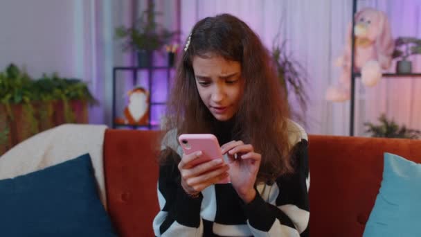 十几岁的女孩使用智能手机打字浏览 失去了成为惊喜突然彩票结果 坏消息 运气损失 玩游戏失败 小孩子 小孩在家里的夜房里 坐在橙色的沙发上 — 图库视频影像