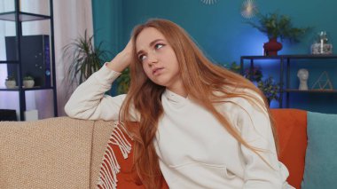 Portrait of sad girl sitting at home looks pensive thinks over life concerns or unrequited love, suffers from unfair situation. Young woman problem, break up, depressed feeling bad annoyed, burnout