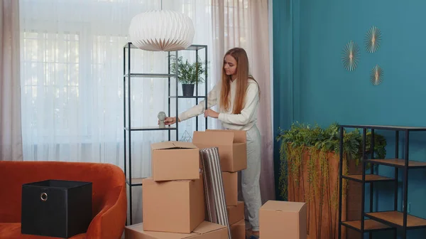 Woman entering room holding cardboard boxes, unpacking packages with interior stuff furniture after rental or buying new apartment home house. Girl concentrated on moving relocation. People lifestyle