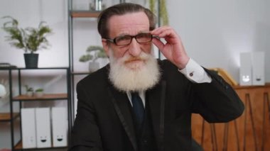 Gözlüklü mutlu kıdemli işadamı ofis masasında gülümseyen kameraya bakıyor. Yaşlı büyükbabanın portresi. Serbest çalışan bir girişimci. Şirket lideri.