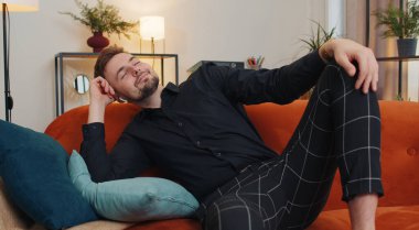 Kablosuz kulaklıklı genç adam evdeki koltukta uzanıyor ve en sevilen disko rock n roll müziğini kulaklıkla dinliyor. İnsanlar hafta sonu aktiviteleri. Çok mutlu bir adam