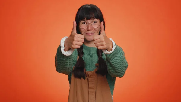 穿着绿色毛衣的书呆子女人竖起大拇指同意某事或给予肯定的回答推荐广告喜欢好的 在橙色工作室背景下孤身一人的小女孩 — 图库照片
